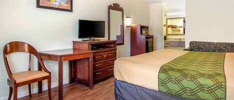 A hotel room with a wooden desk, a television, a bed with a patterned bedspread, a mirror, and a dresser.