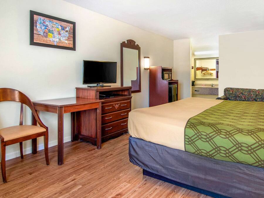 Une chambre d’hôtel avec un bureau en bois, une télévision, un lit avec une couvre-lit à motifs, un miroir et une commode.
