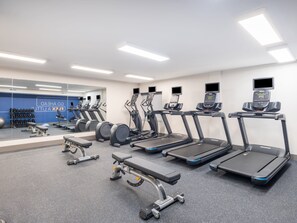 Een fitnessruimte met loopbanden, elliptische trainers en losse gewichten.