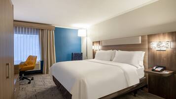 A hotel room with a large bed, a desk with a chair, a bedside table with a phone, and a window with curtains.