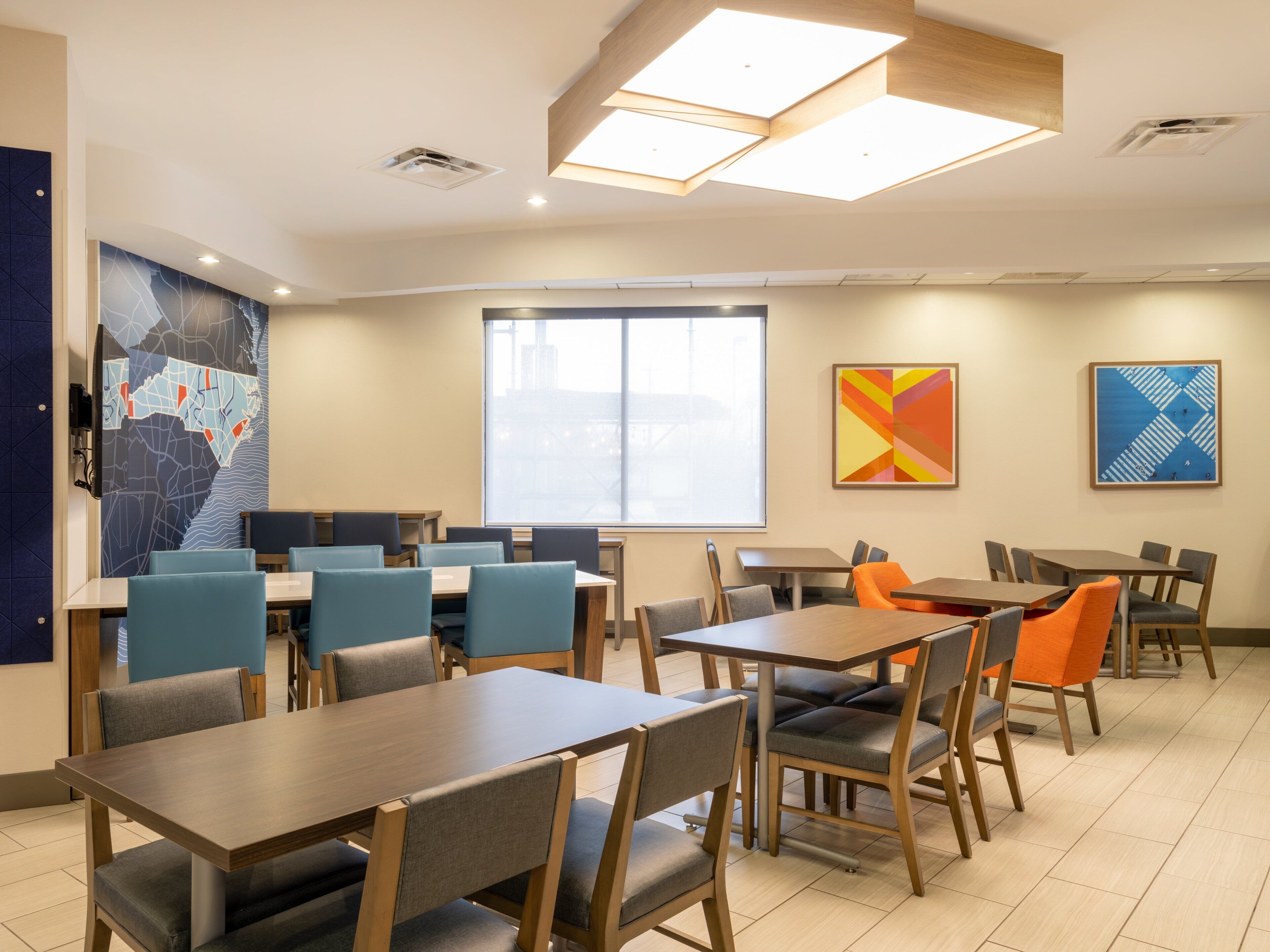 A modern dining area with multiple tables and chairs, a large window, and abstract wall art.