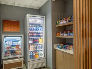 Een automaat met diverse snacks en drankjes, een vriesvak met diepvriesproducten, en een plank met verpakte waren.