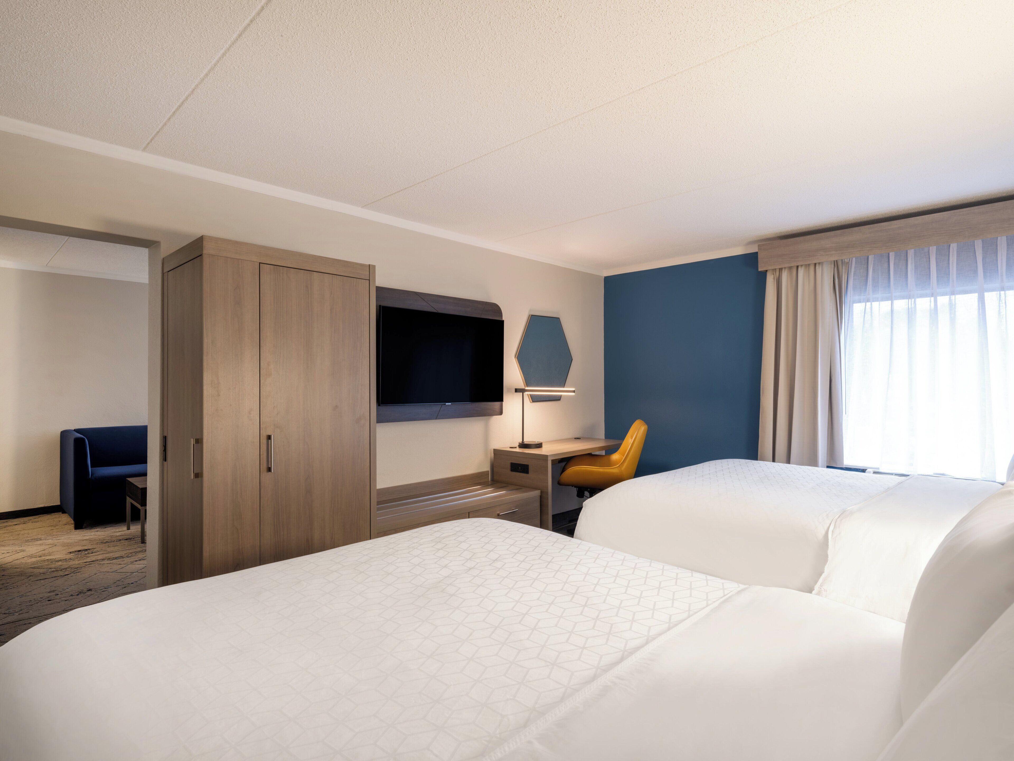 A hotel room with two beds, a desk, a chair, a TV, and a wardrobe.