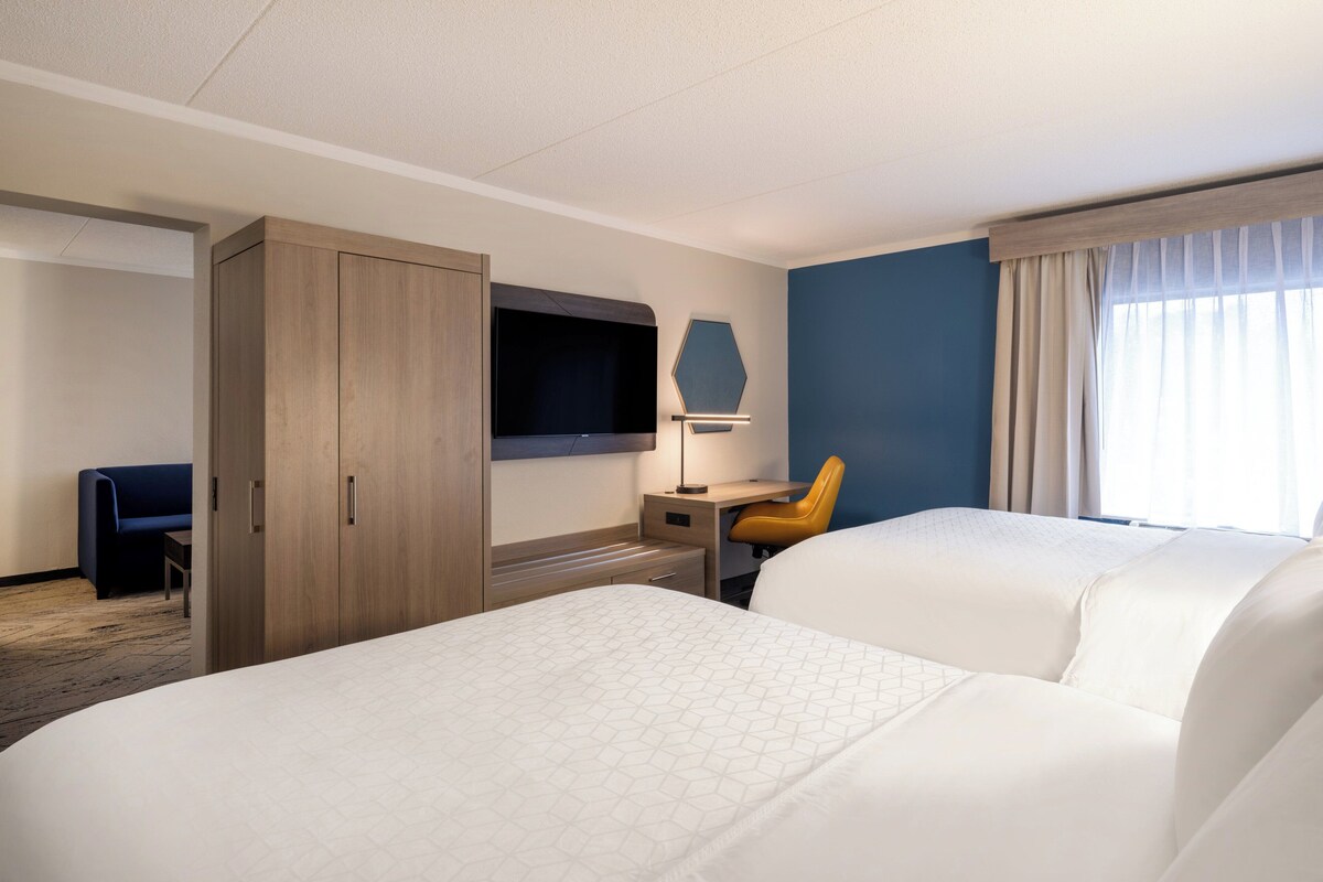 Een hotelkamer met twee bedden, een bureau met stoel, een aan de muur bevestigde televisie en een kledingkast.