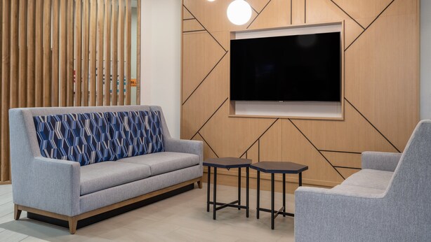 Un salon moderne avec un canapé gris, un coussin décoratif à motifs, un téléviseur à écran plat fixé à un mur en bois et une petite table.