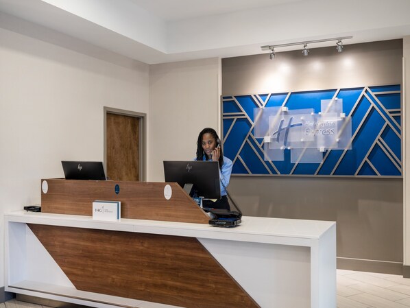 Un mostrador de recepción de hotel con dos computadoras, detalles de madera y un diseño mural geométrico azul.