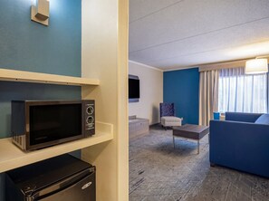 A hotel room with a microwave, a small refrigerator, a sofa, a chair, and a television. - Holiday Inn Express & Suites Greensboro-(I-40 Wendover) by IHG (Greensboro)