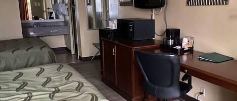 Une chambre d’hôtel équipée d’un lit, d’un bureau avec un ordinateur, d’une chaise, d’une télévision et d’une machine à café.
