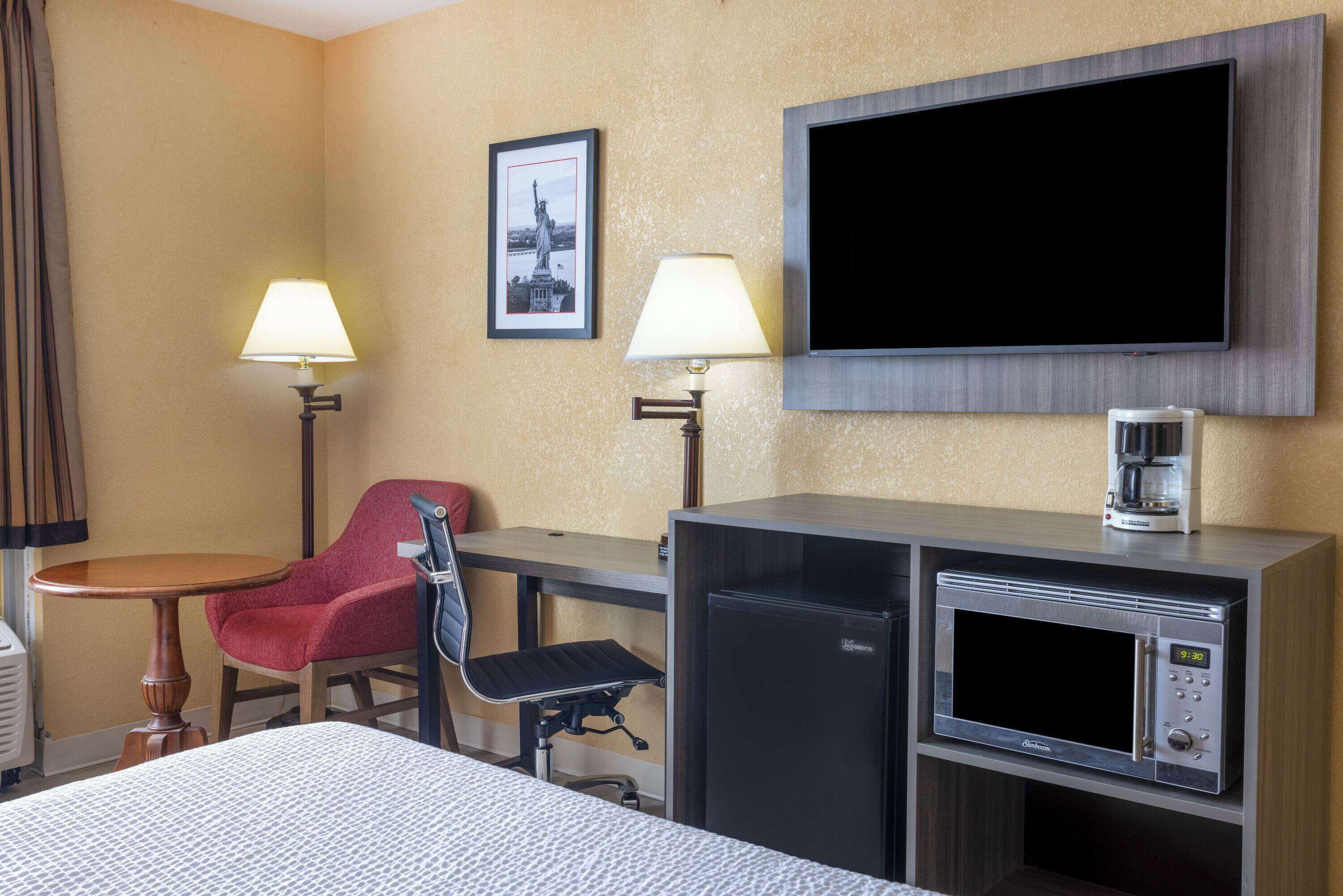 A hotel room with a bed, a desk with a chair, a TV mounted on the wall, a coffee maker, and a microwave.