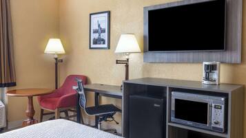 A hotel room with a bed, a desk with a chair, a TV mounted on the wall, a coffee maker, and a microwave.