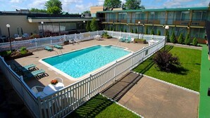 A rectangular swimming pool with a white fence surrounding it, a grassy area, and a building with multiple windows in the background. - Ramada by Wyndham Rome / Verona (Rome)