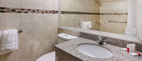 A bathroom with a granite sink, white toilet, and a mirror reflecting the shower area.