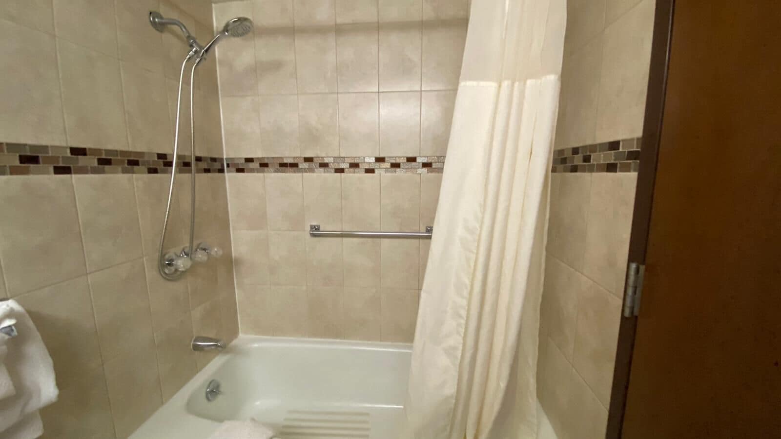 A shower with a handheld showerhead, a glass-enclosed tub, and a towel rack.
