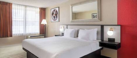 A hotel room with a large bed, bedside lamps, a wall-mounted mirror, and a window with curtains.