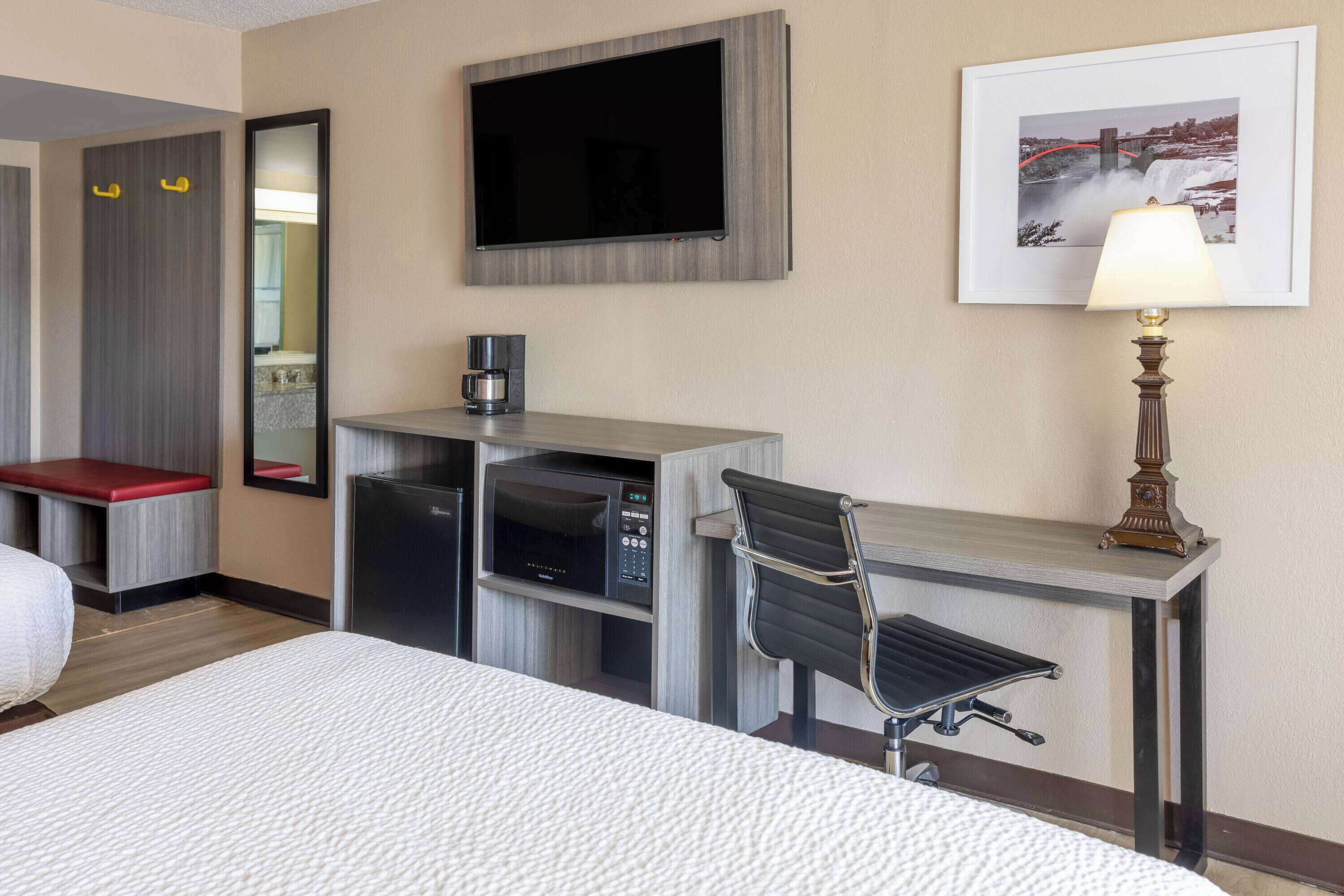 A hotel room with a bed, a desk with a chair, a television, a coffee machine, and a lamp.