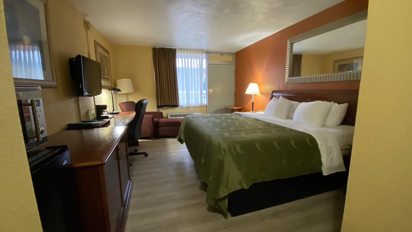 A hotel room with a bed, desk, chair, and a television.