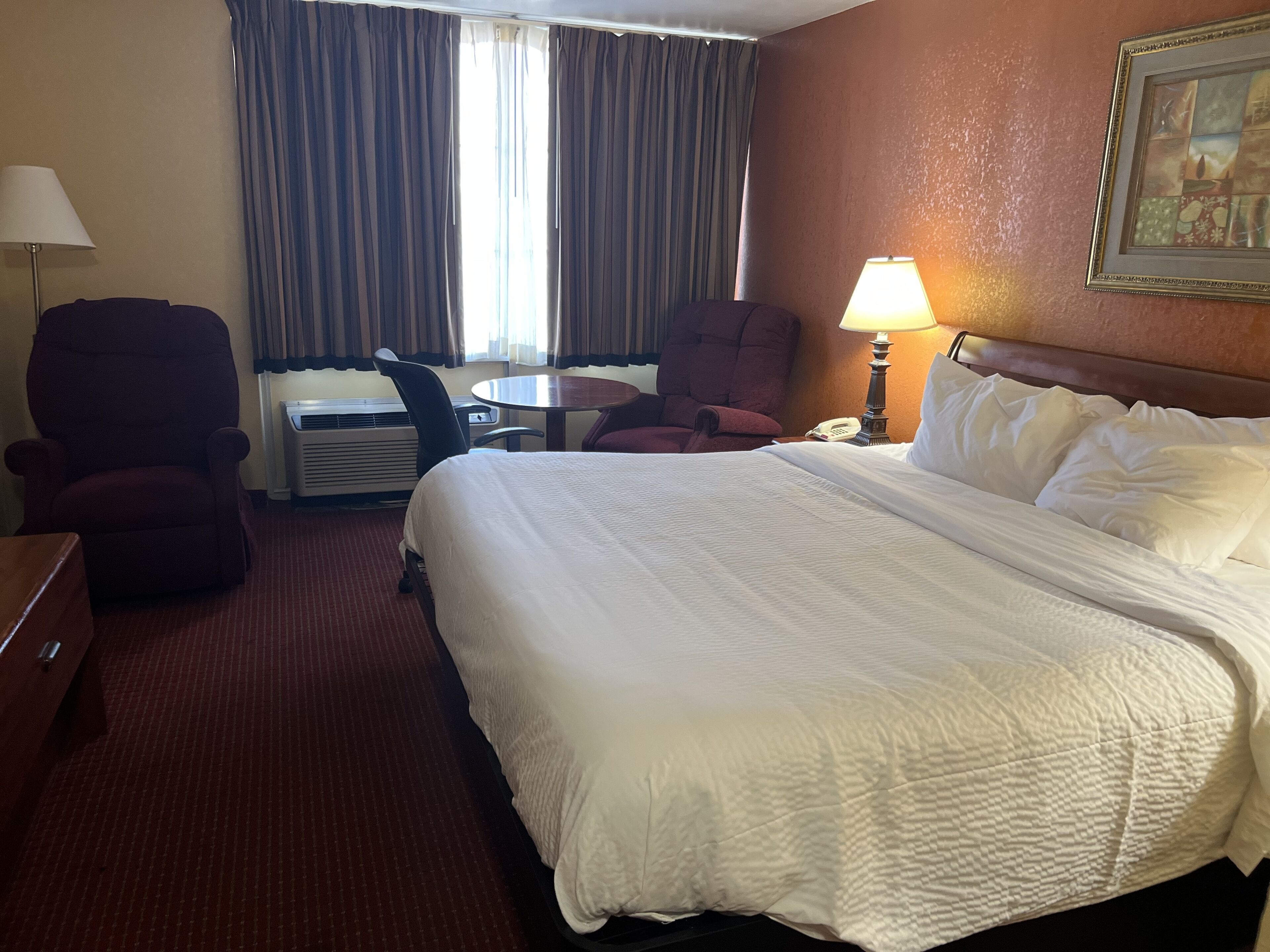 A hotel room with a large bed, two armchairs, a desk, a lamp, and a painting on the wall.