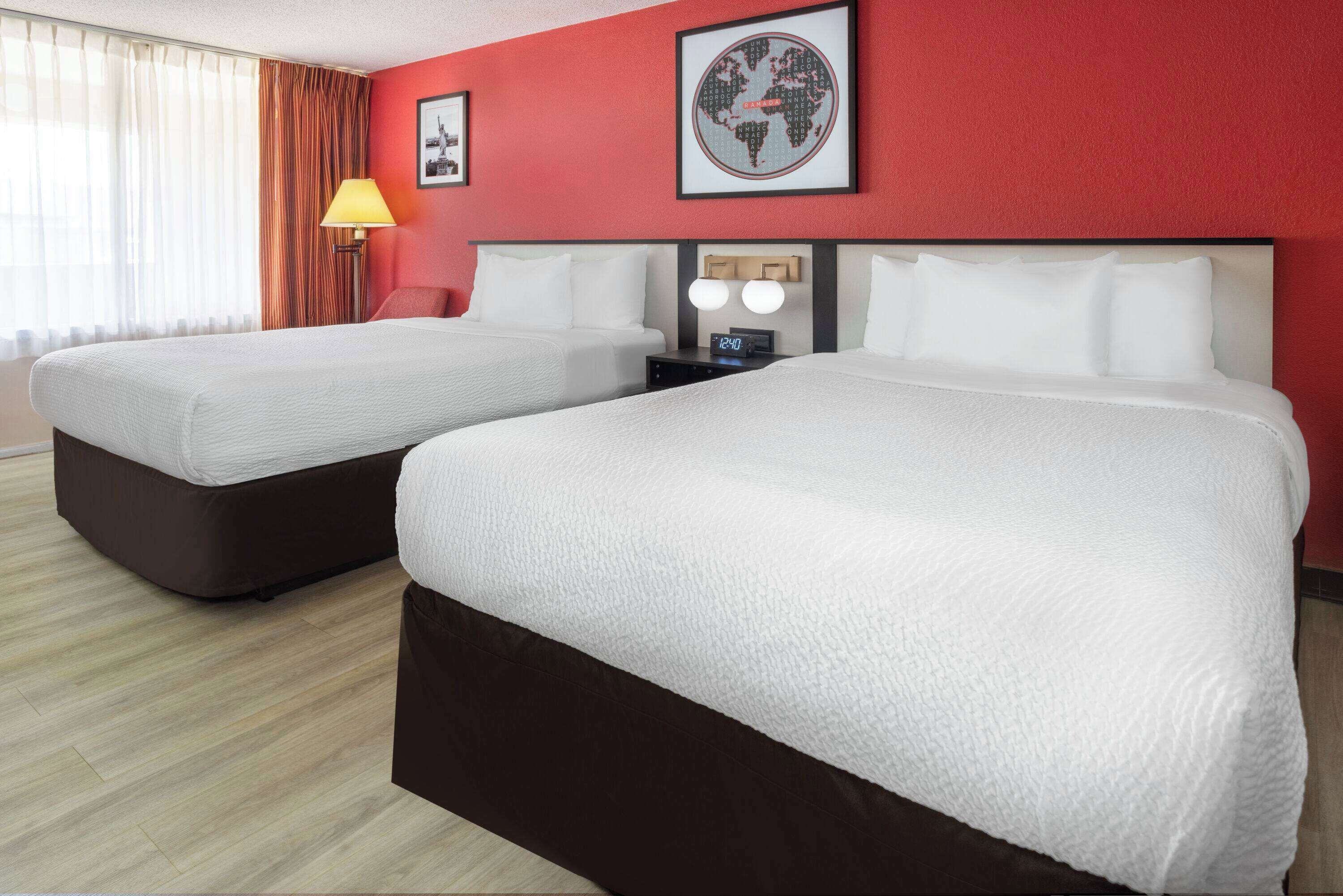 Habitación de hotel con dos camas, una pared roja, una obra de arte con un globo terráqueo y un reloj.