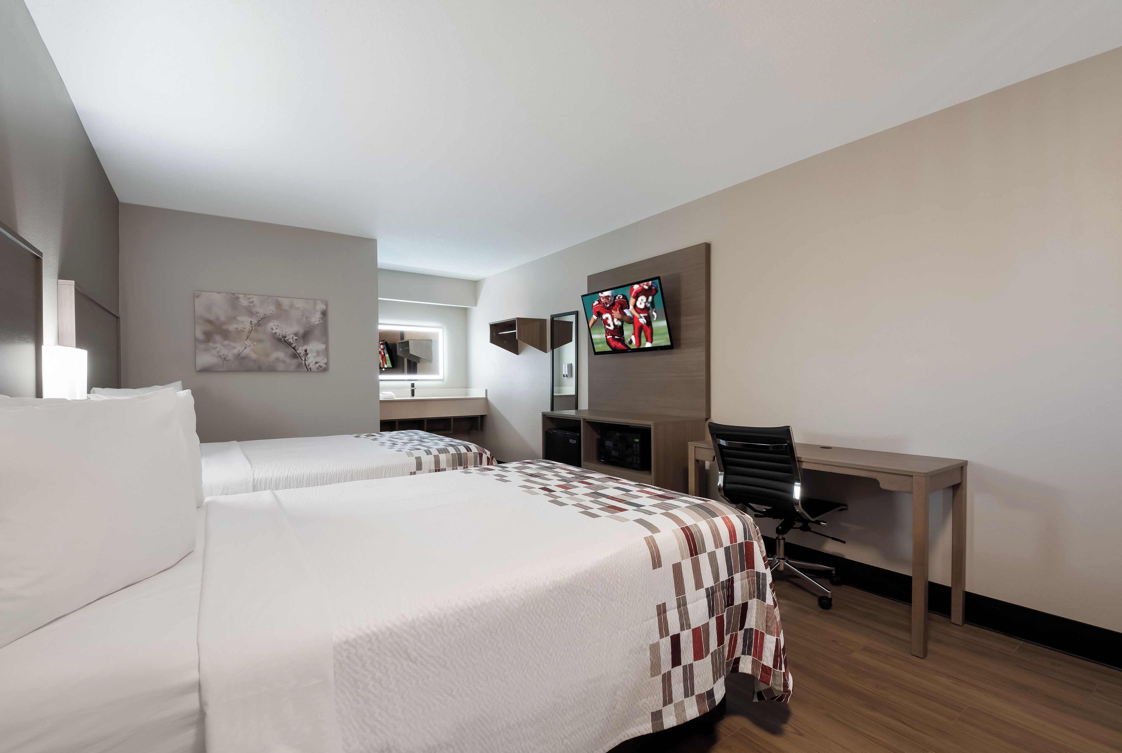 Habitación de hotel con dos camas, un escritorio, una silla, un televisor y una ventana.