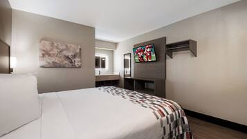 A hotel room with a bed, a TV mounted on the wall, a mirror, and a painting.