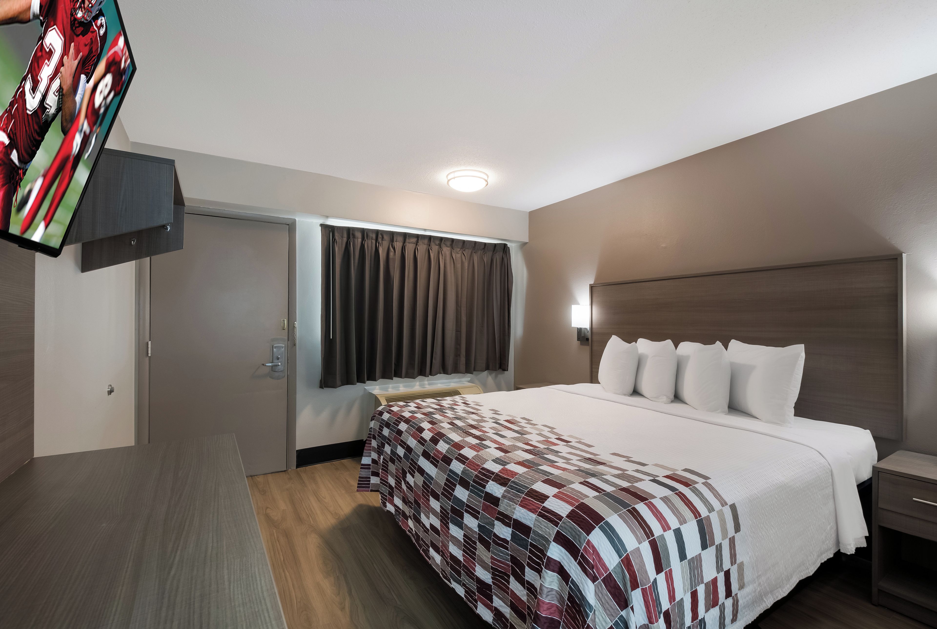 A hotel room with a bed, a desk, a TV, and a window with curtains.