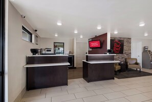 Un espace d’accueil d’hôtel doté d  ’un écran numérique affichant la mention « Wi-Fi gratuit dans toutes les chambres », d’un comptoir d’accueil, d’un mur décoratif en pierre et d’un distributeur automatique de billets.