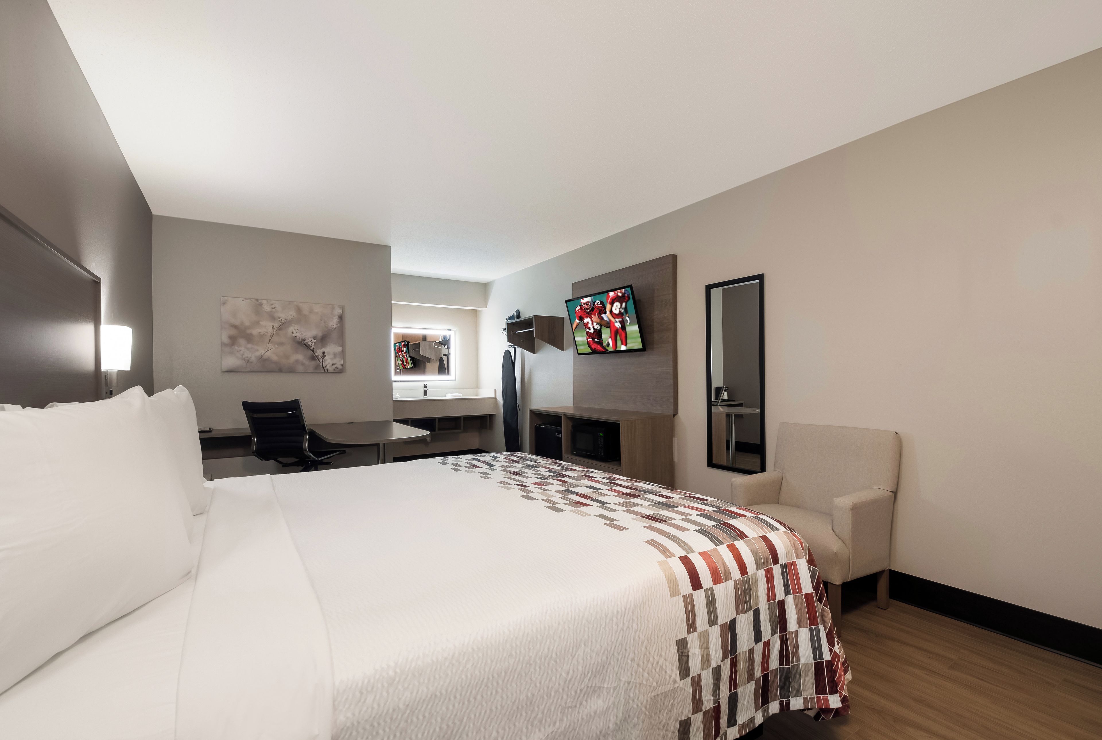 Habitación de hotel con una cama grande, un escritorio, una silla, un televisor y un cuadro en la pared.