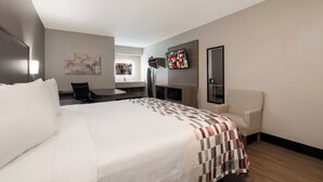 Quarto de hotel com uma cama grande, escrivaninha, cadeira, televisão e um quadro na parede.