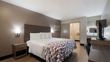 A hotel room with a bed, a nightstand, a desk with a computer, a mirror, and a shower area.