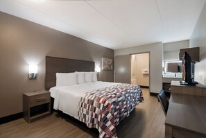 A hotel room with a bed, a nightstand, a desk with a computer, a mirror, and a shower area. - Red Roof Inn Chattanooga - Hamilton Place (Chattanooga)