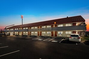 Ett motell med en parkeringsplats, en skylt som visar att det är ett Red Roof Inn, och en vit bil som står parkerad på platsen.