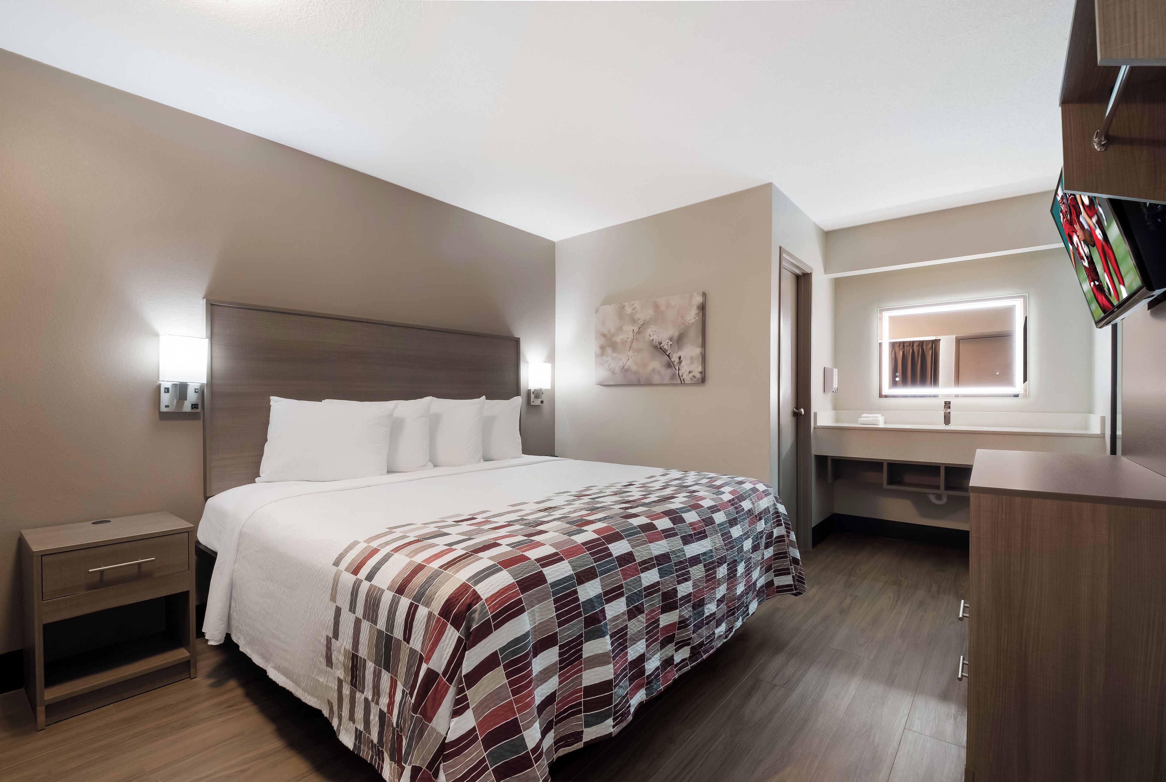 A hotel room with a bed, bedside table, a mirror, and a television.