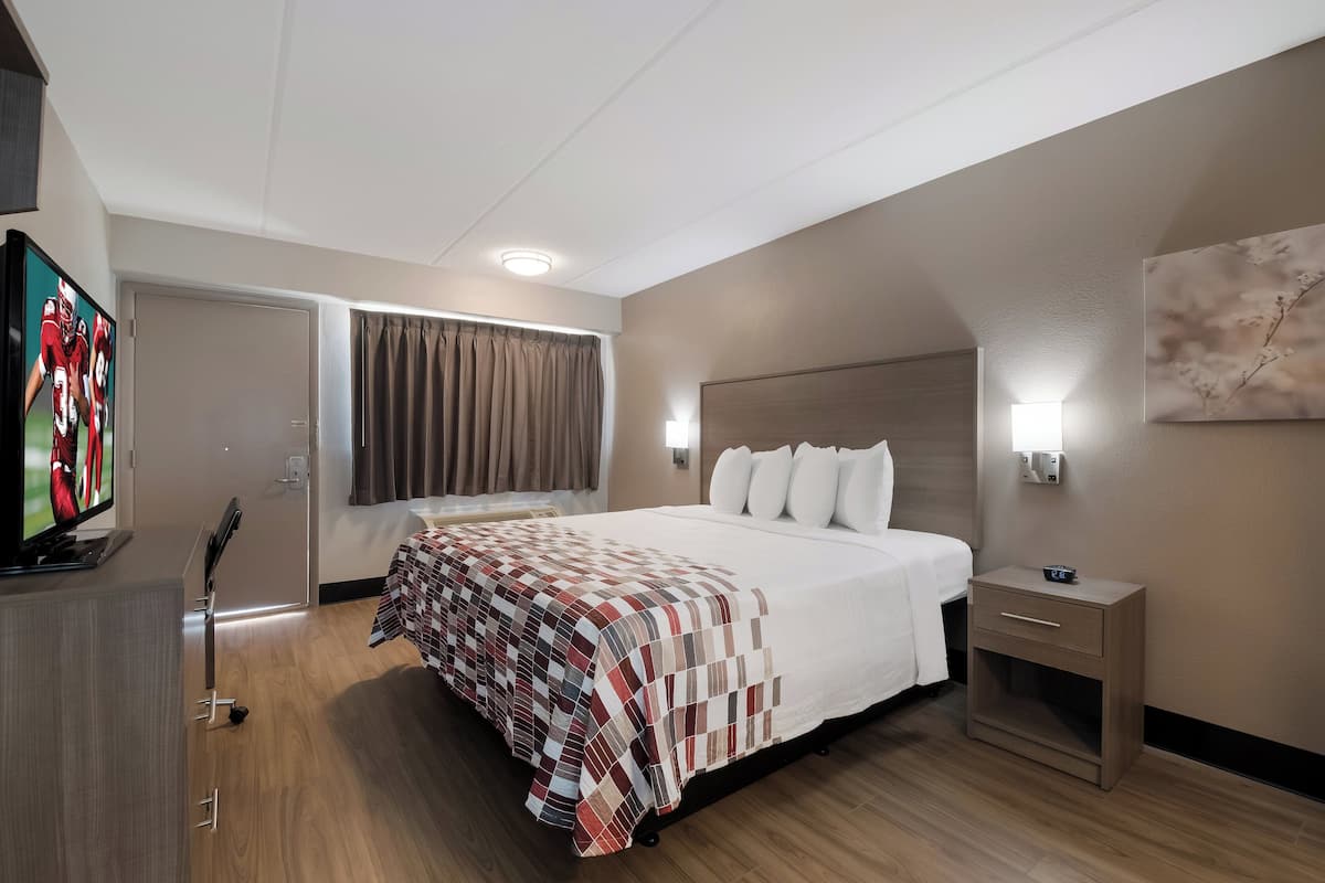 Hotellihuone, jossa on sänky, yöpöytä, televisio ja taulu seinällä.