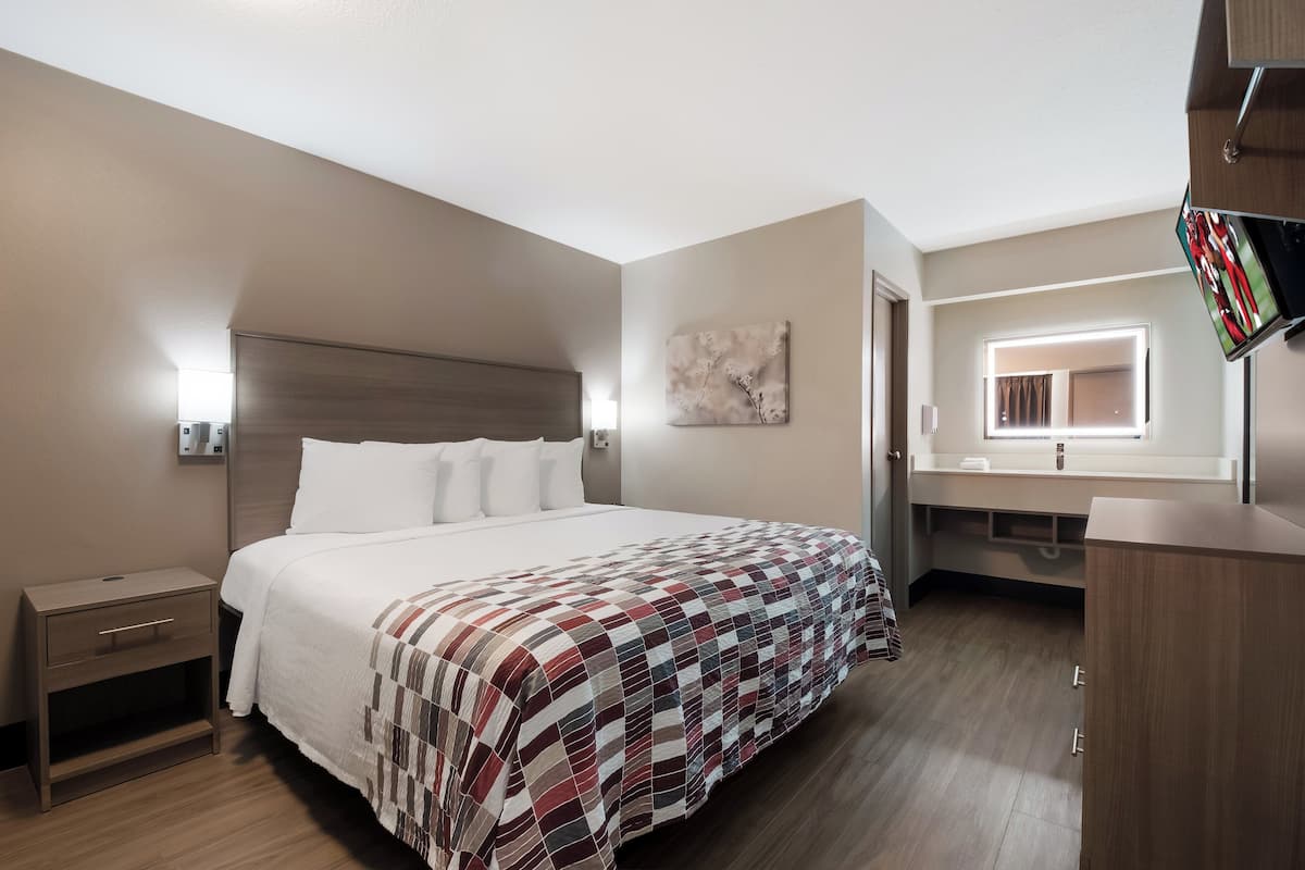 Hotellihuone, jossa on sänky, yöpöytä, lipasto, peili ja ikkuna.