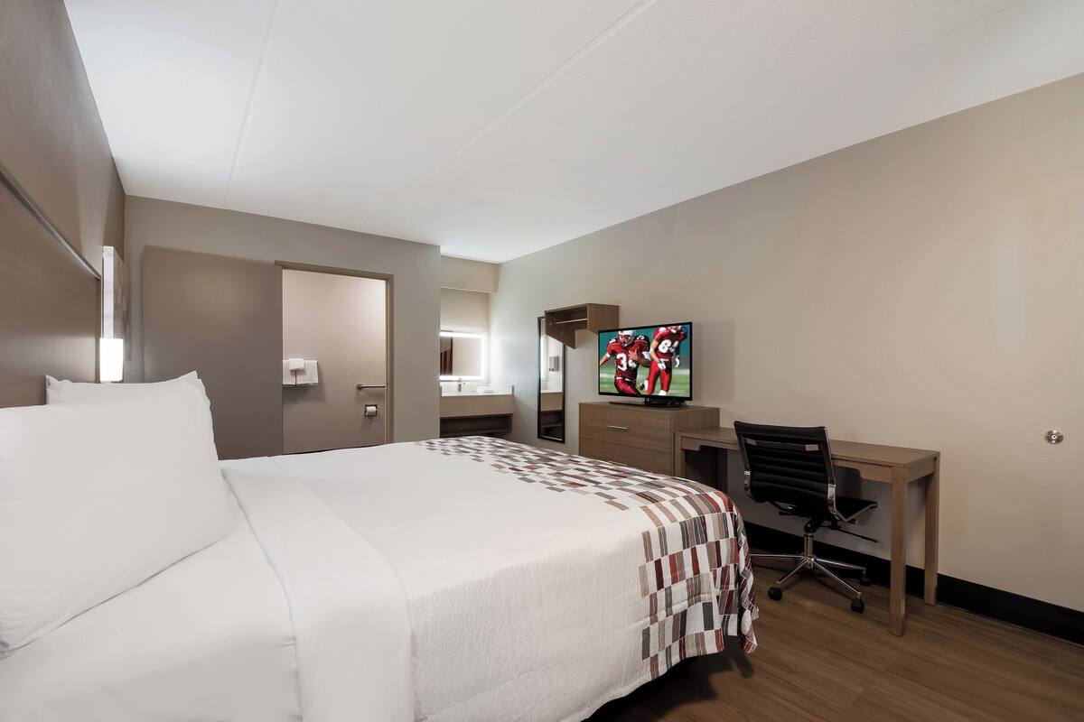 A hotel room with a bed, a desk, a chair, a television, and a mirror.