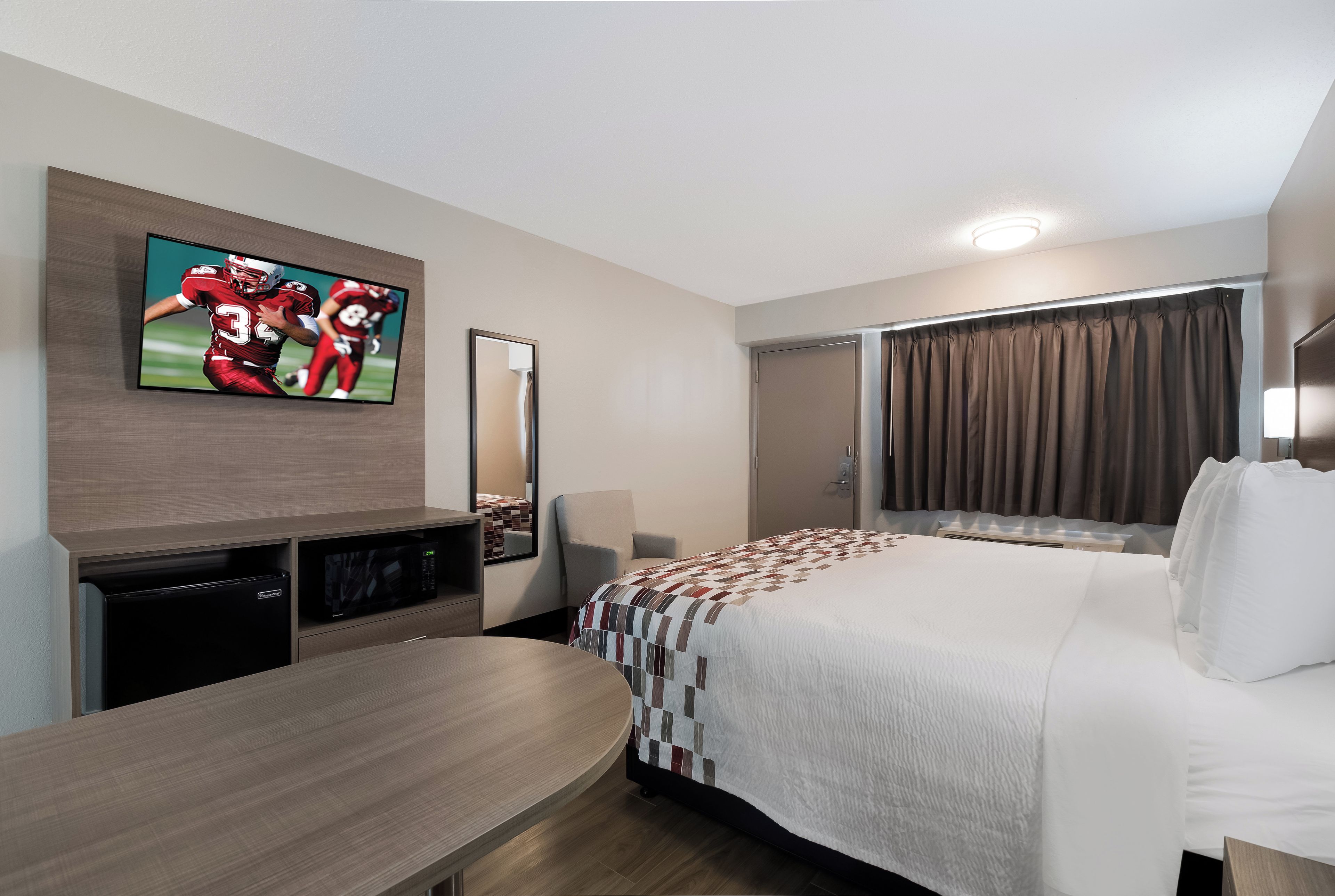A hotel room with a bed, a desk, a television, a mirror, and a door.