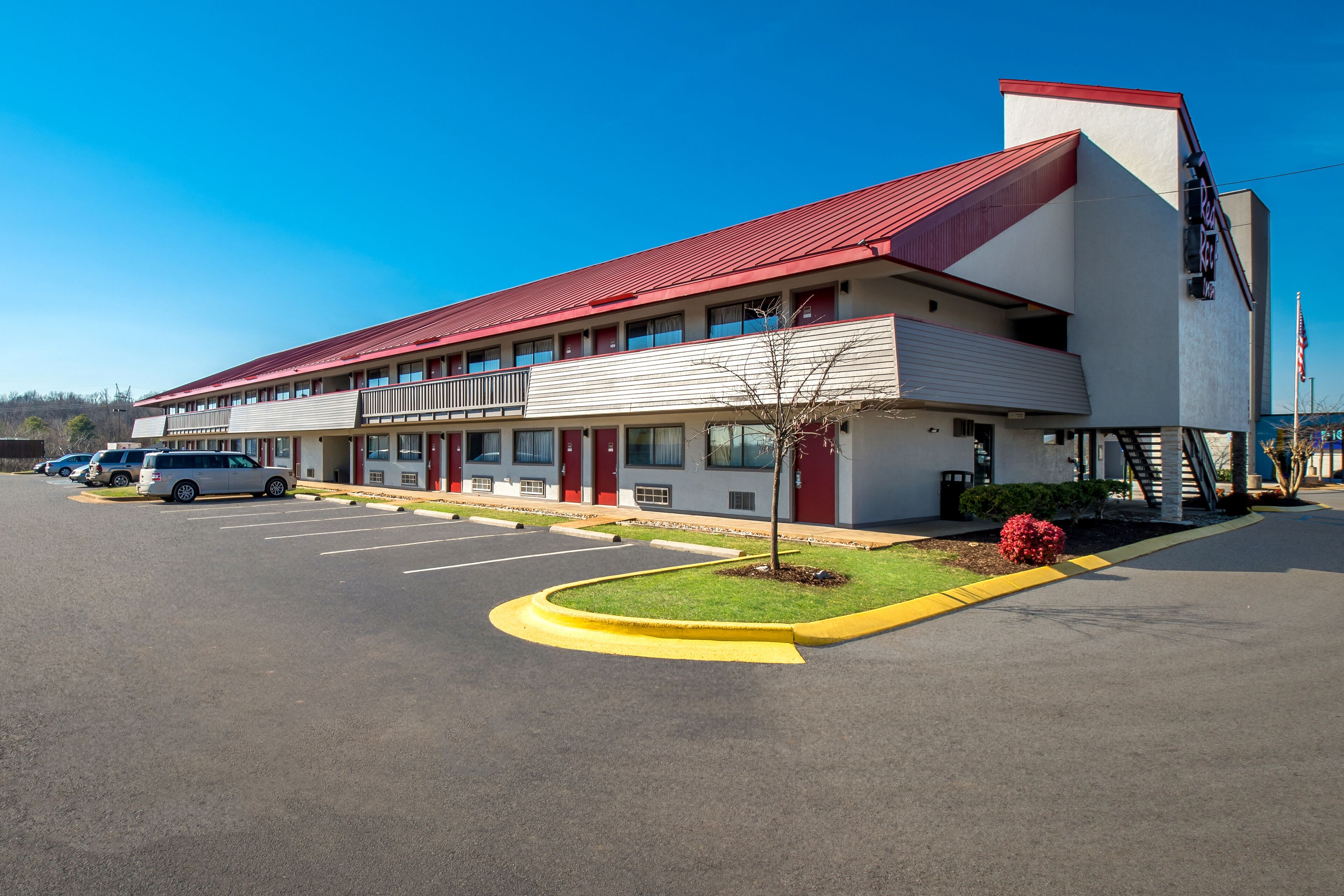 A motel with a red roof, multiple balconies, and a parking lot.