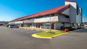 A motel with a red roof, multiple balconies, and a parking lot.
