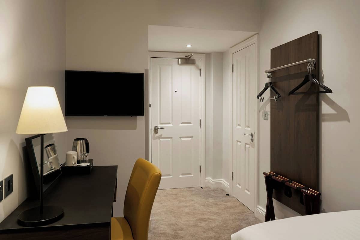 Ein Hotelzimmer mit einem Bett, einem Schreibtisch mit Lampe, einem Fernseher und einem Kleiderständer.