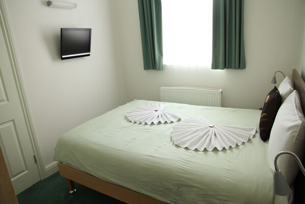 A neatly made bed with a light green bedspread and two decorative white pillows. A flat-screen TV is mounted on the wall above the bed. - Four Points Flex by Sheraton London Kensington Olympia (London)