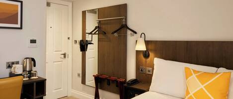 A hotel room with a bed, a desk with a coffee maker, a mirror, and a coat rack.