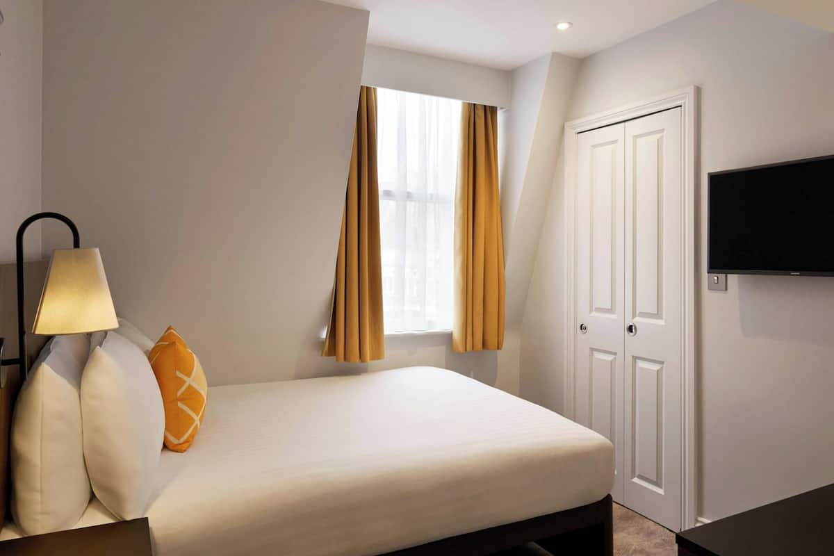 Ein Hotelzimmer mit Bett, Wandfernseher und einem Vorhangfenster.