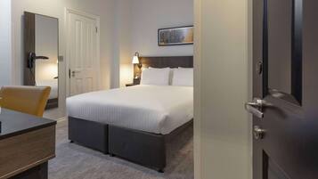 A hotel room with a bed, bedside table, chair, and a door.