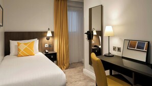 Ein Hotelzimmer mit einem Bett, einem Schreibtisch, einem Stuhl, einem Spiegel, einer Lampe und einem Bilderrahmen.