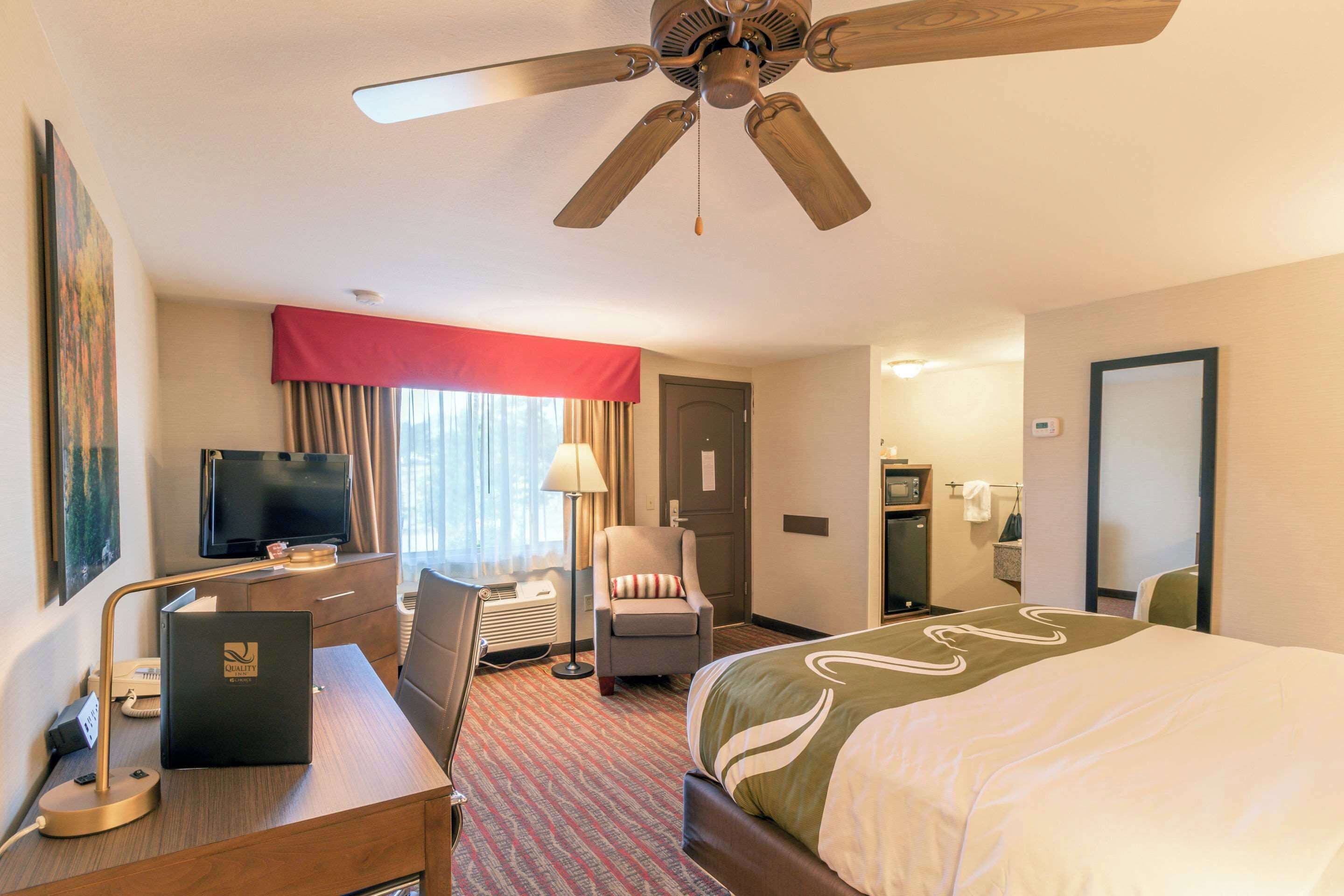 Une chambre d’hôtel équipée d’un lit, d’un bureau, d’une chaise, d’une télévision et d’un ventilateur de plafond.