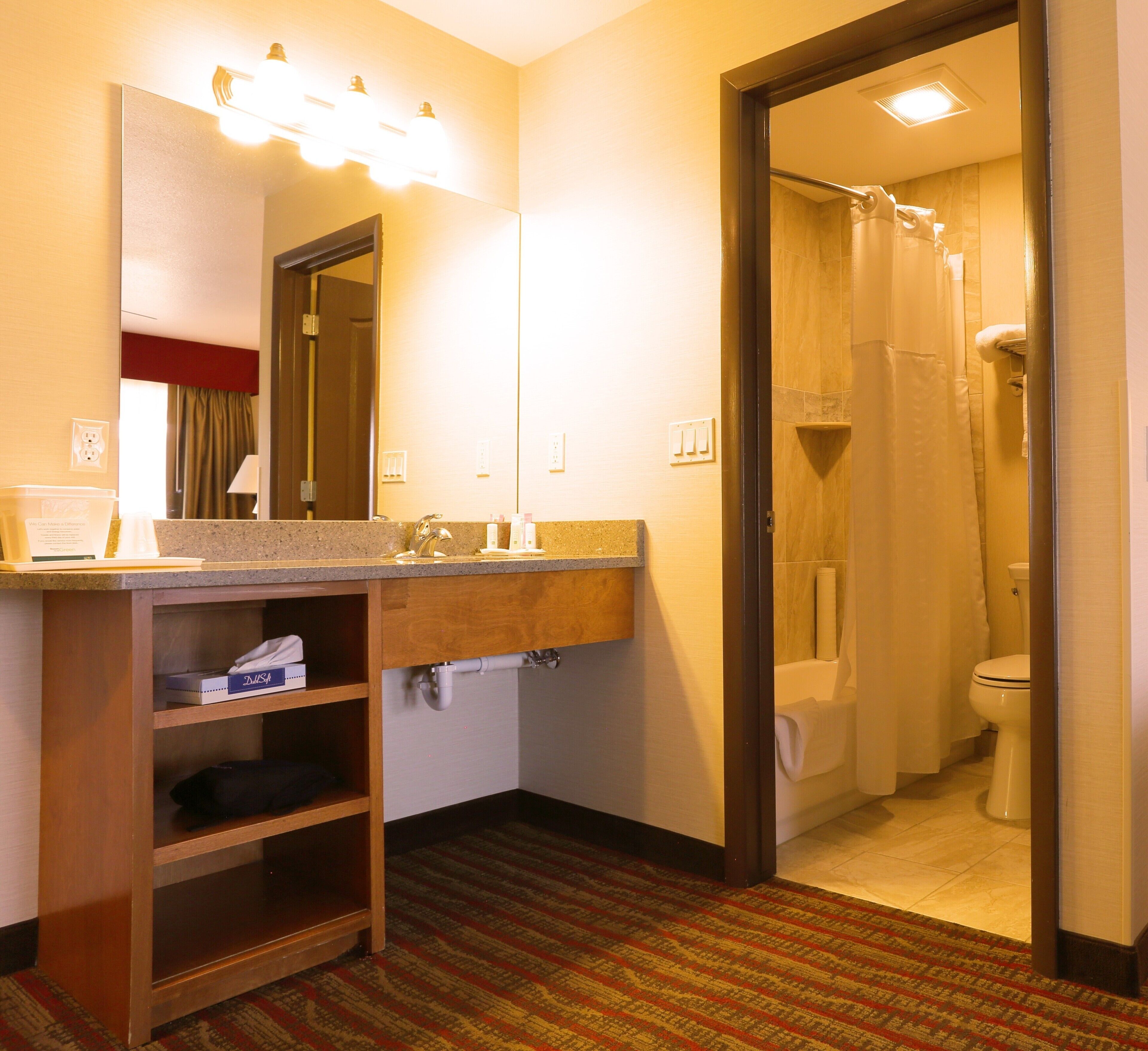 A hotel bathroom with a sink, mirror, shower, and toilet.