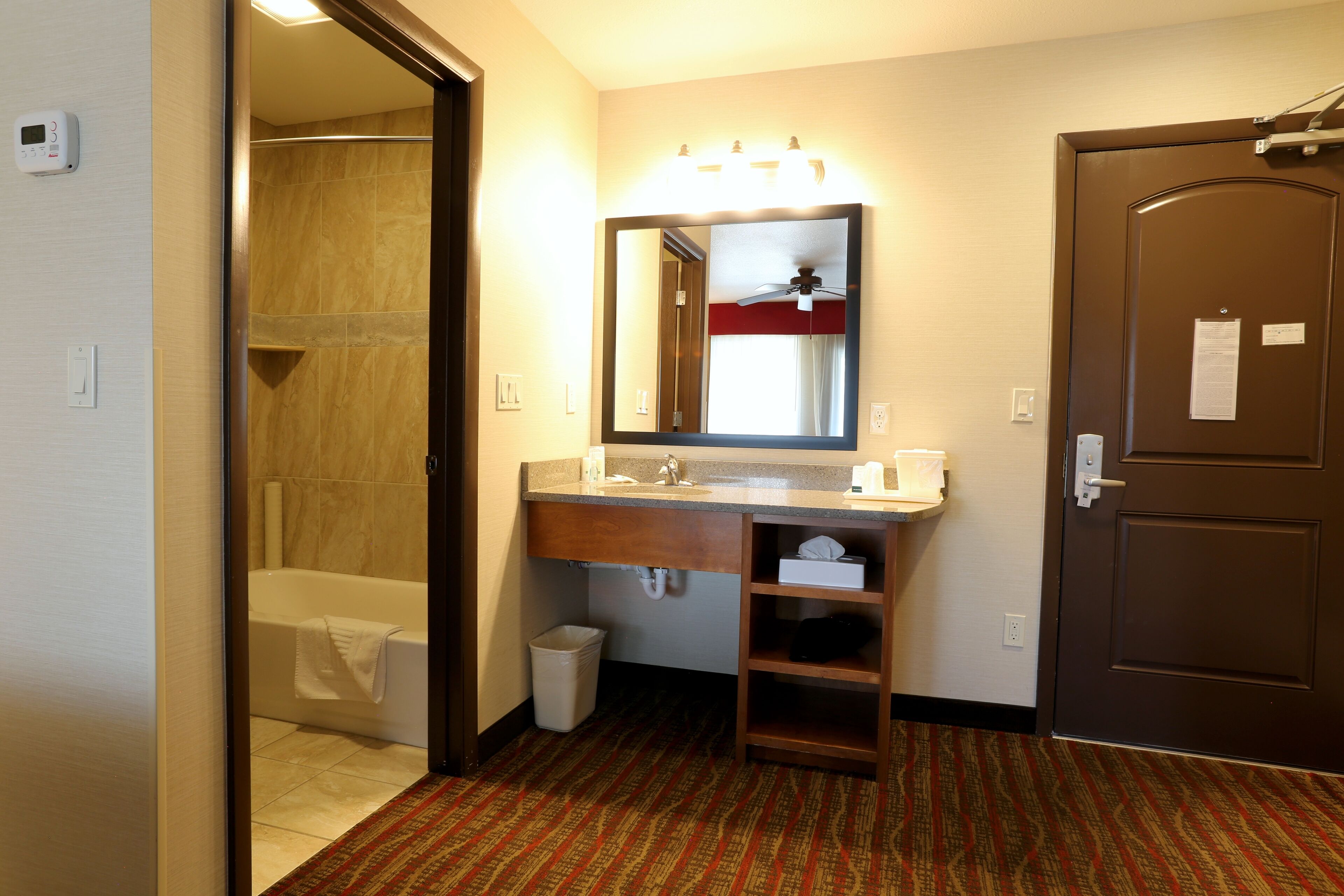 A hotel bathroom with a shower, sink, mirror, and a door.