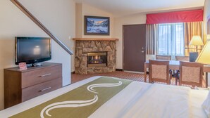 A hotel room with a fireplace, a television on a wooden cabinet, a dining area with chairs, and a bed with a green and white blanket. - Quality Inn near Rocky Mountain National Park (Estes Park)