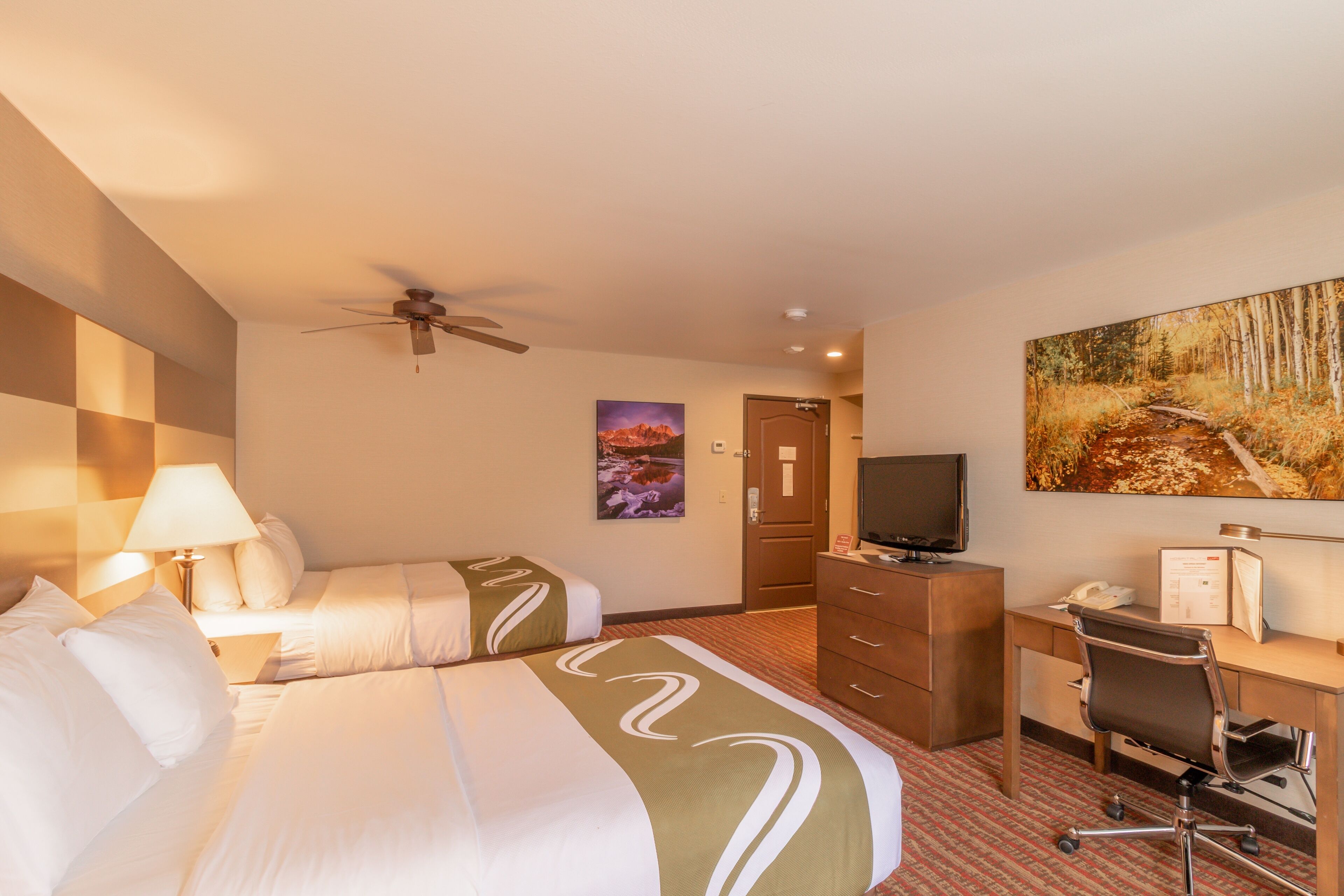 A hotel room with two beds, a desk, a chair, a television, and a painting on the wall.