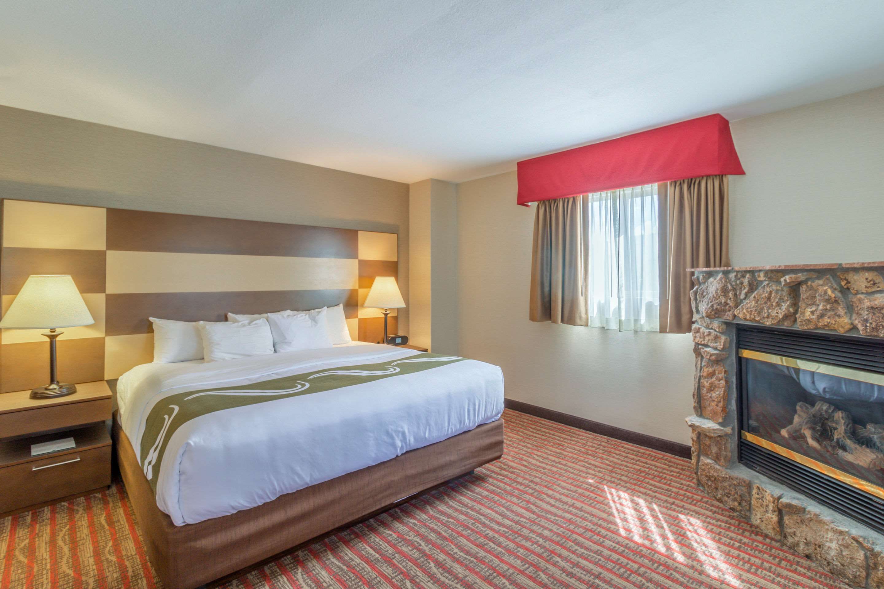 Une chambre d’hôtel avec un grand lit, deux tables de chevet avec des lampes, une cheminée et une fenêtre avec des rideaux.